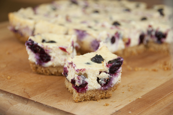 Creamy lemon cheesecake bars recipe swirled with blueberries on a simple graham cracker crust.