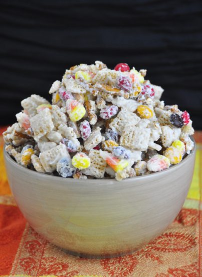 A new twist on party snack mix includes white chocolate, chex cereal, fall M&M's, candy corn, and pretzel sticks for a Halloween dessert.