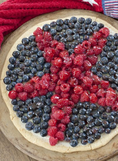 Patriotic Sugar Cookie Fruit Pizza dessert recipe will be the star (no pun intended) of the show at your summer 4th of July party! Fresh, colorful fruit and sweet cream cheese filling give this cookie pizza the perfect combination of pretty and tasty.