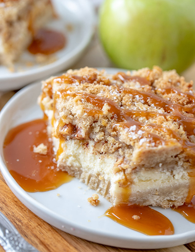 Quick & Easy Salted Caramel Apple Cheesecake Bars is a great fall baking recipe with a shortbread crust, cheesecake filling, and an irresistible streusel topping. The salted caramel drizzle makes these the perfect fall dessert for Thanksgiving or Christmas!