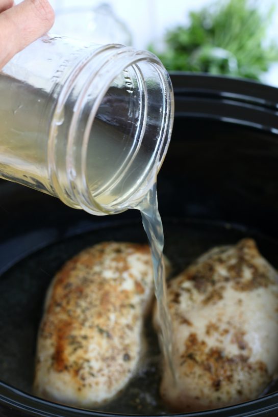 Pouring chicken stock into a crockpot to add flavor to the chicken in alfrdo sauce.