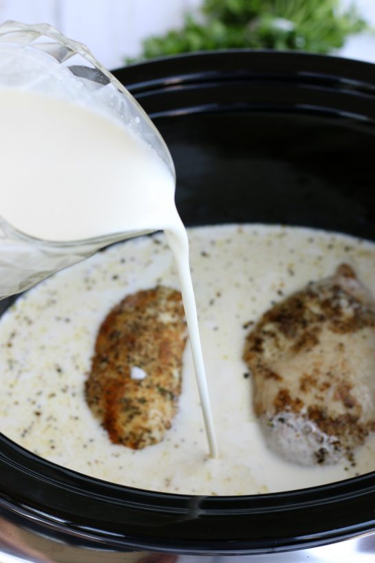 Pouring creamy alfredo sauce into the slow cooker for chicken alfredo.