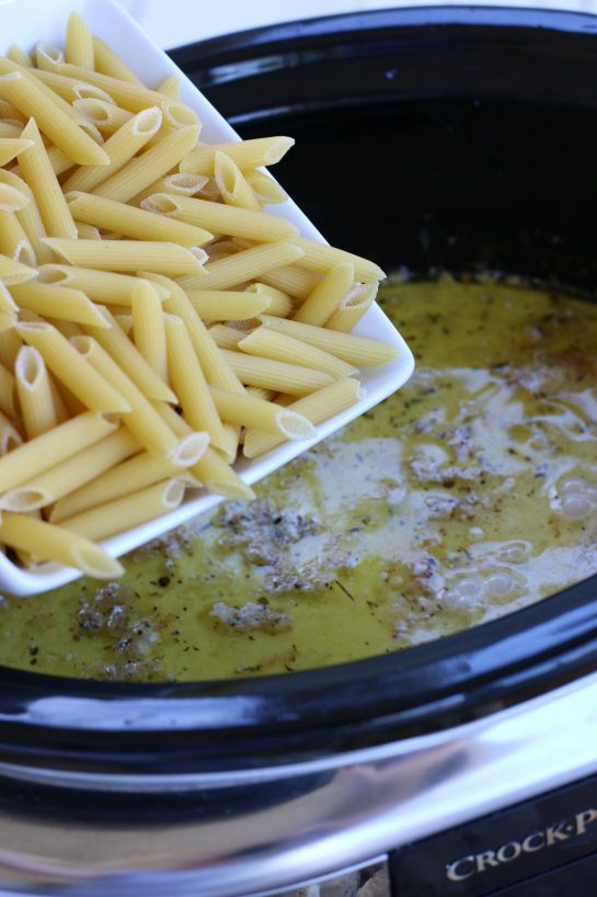 Adding penne pasta to the alfredo sauce in a crock pot.