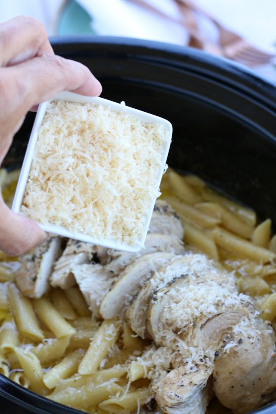 Sprinkling freshly grated Parmesan cheese on top of a chicken alfredo crock pot recipe.