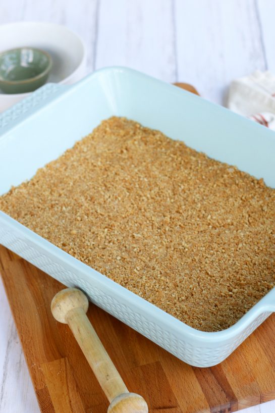 A light blue coloered baking dish with the graham cracker crust for a cheesecake.