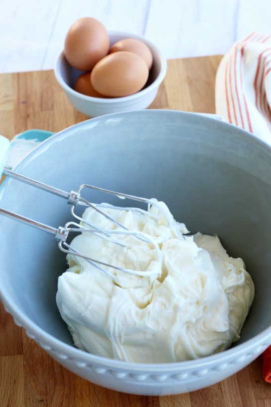 Softened cream cheese whipped with a hand mixer in a blue mixing bowl.