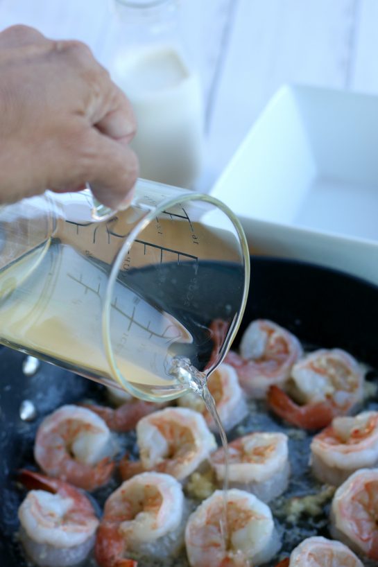Adding the chicken stock to the cooking shrimp to help create the garlic butter sauce.