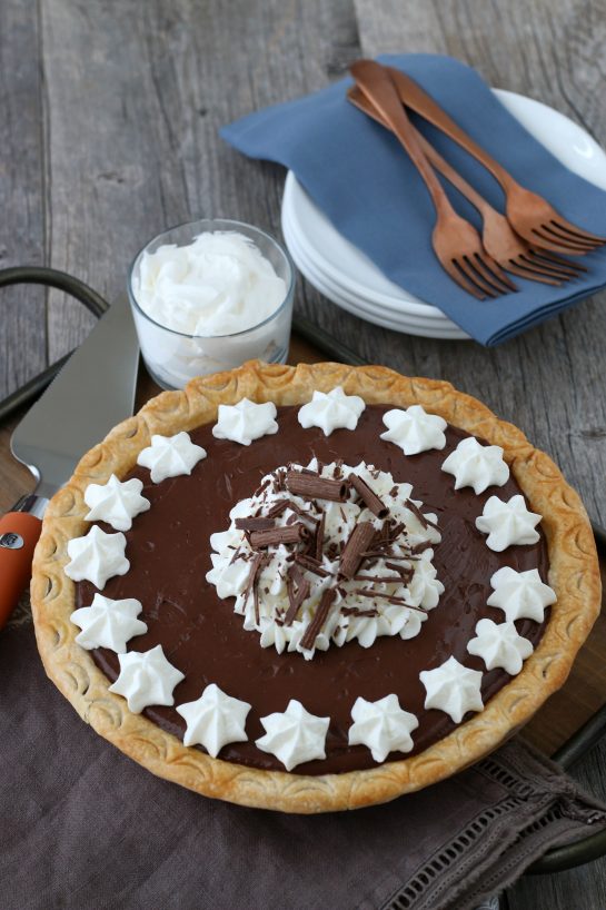 Homemade chocolate pie is the kind of dessert that dreams are made of. It's got homemade chocolate pudding from scratch, perfectly fluffy whipped cream, and it is easier to make than you might think! Finished homemade chocolate pie topped with whipped cream and ready to be eaten.