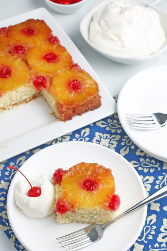 Another view of a slice of the upside down cake recipe on a plate, with whipped cream and fruit!