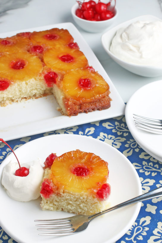 This photo shows us a slice of the pineapple upside down cake from scratch with the rest of the beautiful cake in the background.