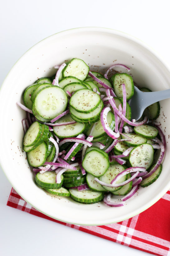 The cucumber salad being made by mixing the cucumber and onions with dressing