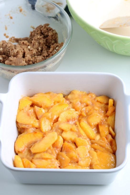 Adding the sliced peaches to the baking pan for the Fresh Peach Crisp recipe