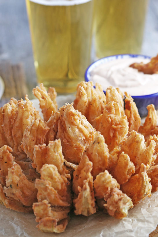 Close-up shot of Fried Blooming Onion with a homemade dipping sauce is the ultimate appetizer recipe. Grab a sweet onion and turn it into a, incredibly delicious appetizer!