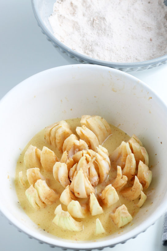 The cut up onion being dipped in the batter for the blooming onion recipe