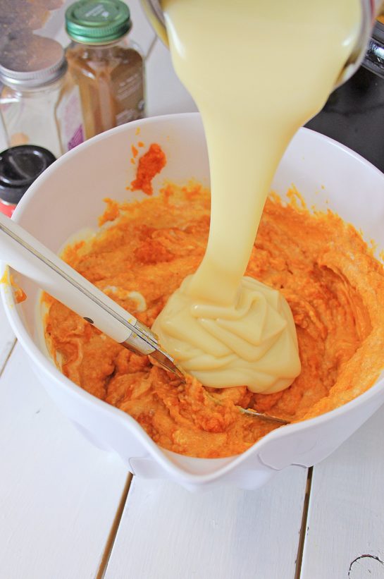 Adding the sweetened condensed milk to the pumpkin mixture for the crock pot pumpkin bread pudding