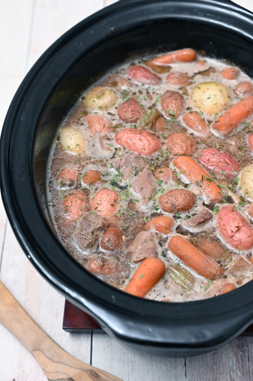 A bowl of savory slow cooker beef stew with thick gravy, potatoes, and peas.
