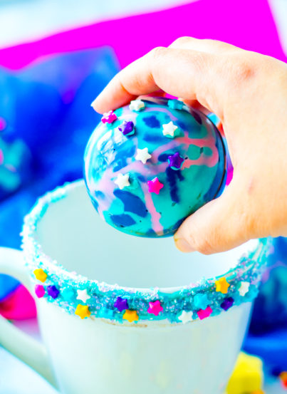 Galaxy Hot Chocolate Bombs are fun, colorful chocolate orbs filled with hot cocoa mix, marshmallows, and sprinkles. This recipe for hot chocolate bombs is an over-the-top way to level up your hot chocolate game, especially for a party!