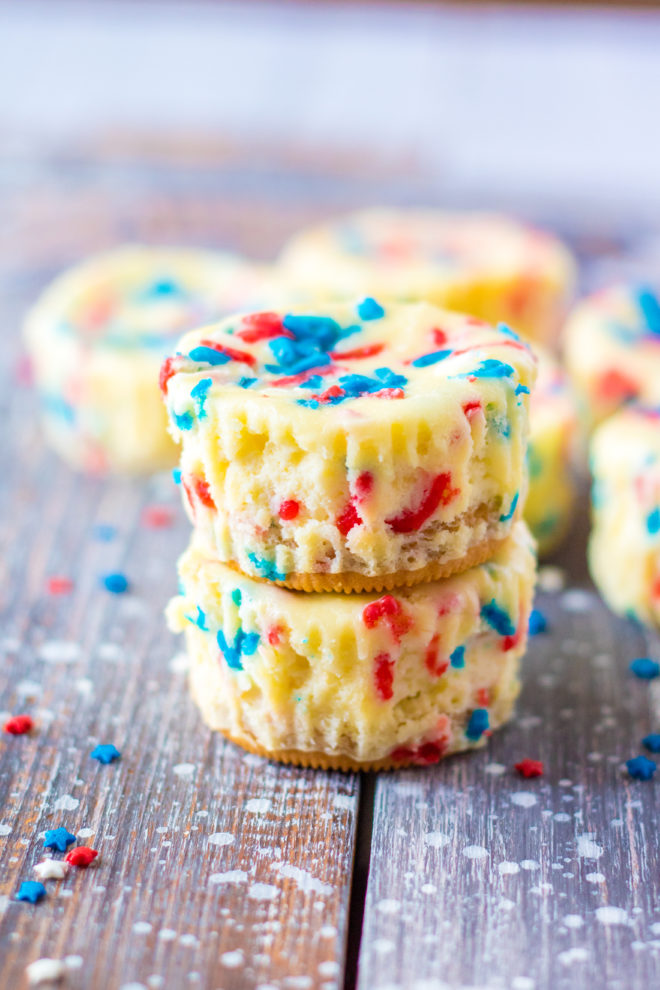 Easy Mini Red, White, and Blue Cheesecakes recipe layered with a Golden Oreo crust and creamy tangy cheesecake. Top with sprinkles and whipped cream for the perfect patriotic dessert for 4th of July!