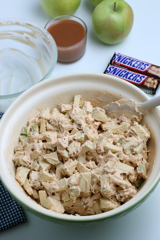 Mixing all of the ingredients for the Caramel Apple Snickers Salad is a delicious side dish recipe with crunchy green apples, marshmallows, and Snickers candy bars as the main ingredients! Perfect for fall holidays and potlucks!