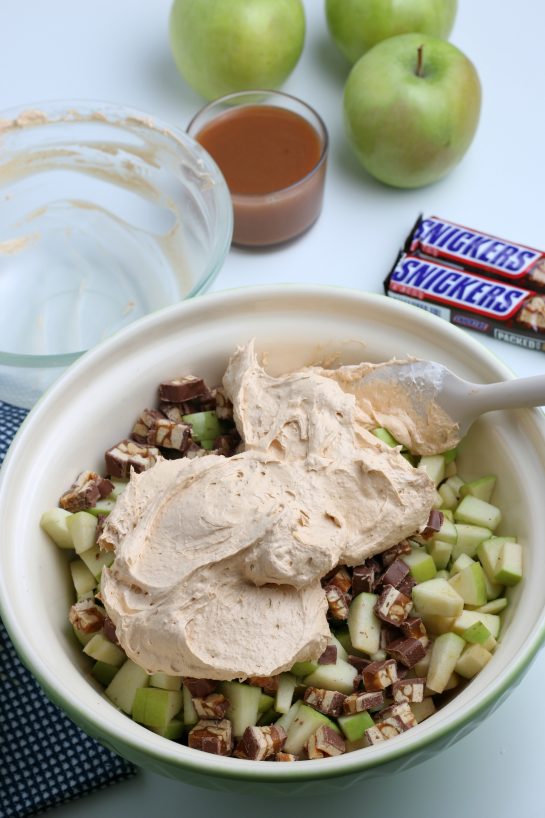 Mixing in the whipped topping with the apples for the Caramel Apple Snickers Salad recipe