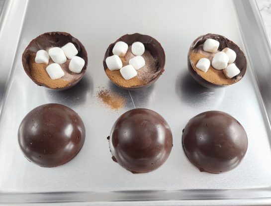 Putting the marshmallows and cocoa into the half spheres out of the molds to make the Mocha Hot Chocolate Bombs recipe 