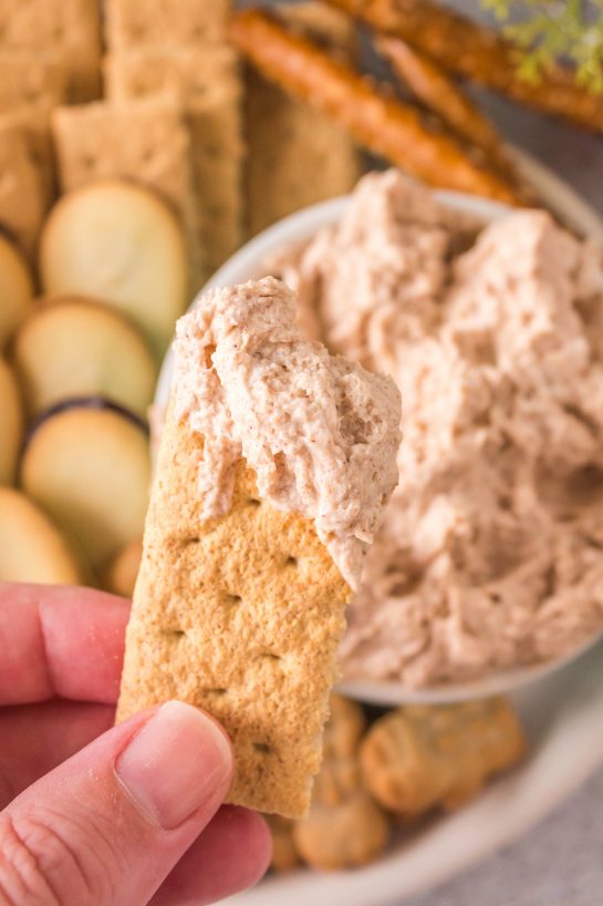 Photo of dipping the graham crackers in the Cinnamon Roll Dip recipe for Christmas