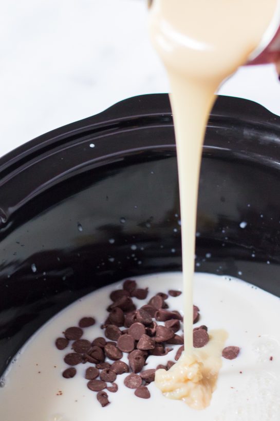 Pouring in the sweetened condensed milk needed for the Slow Cooker Caramel Hot Chocolate recipe