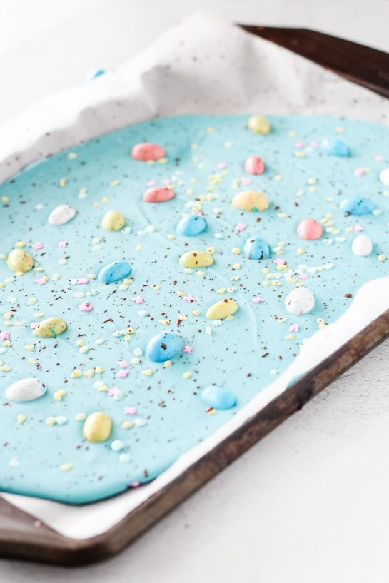 Placing the sprinkles, cocoa powder, and Robin Eggs onto the blue melting chocolate discs for the No-Bake Robin Egg Easter Bark recipe