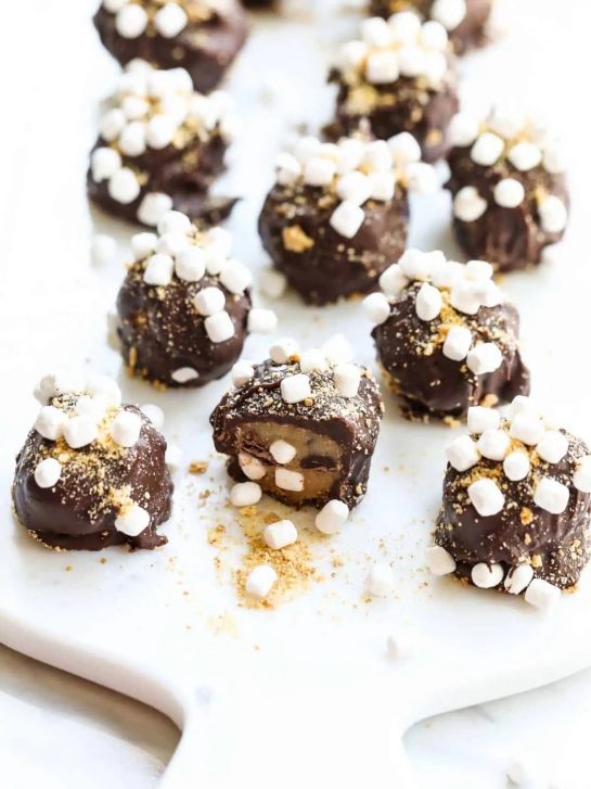 S'more Cookie Dough Truffles are an easy no-bake dessert candy. These have cookie dough studded with chocolate chips and mini marshmallows. Then rolled in crushed graham crackers and a dip into melted chocolate. Each one has sprinkles of mini marshmallows and crushed graham crackers so they taste like campfire s'mores.
