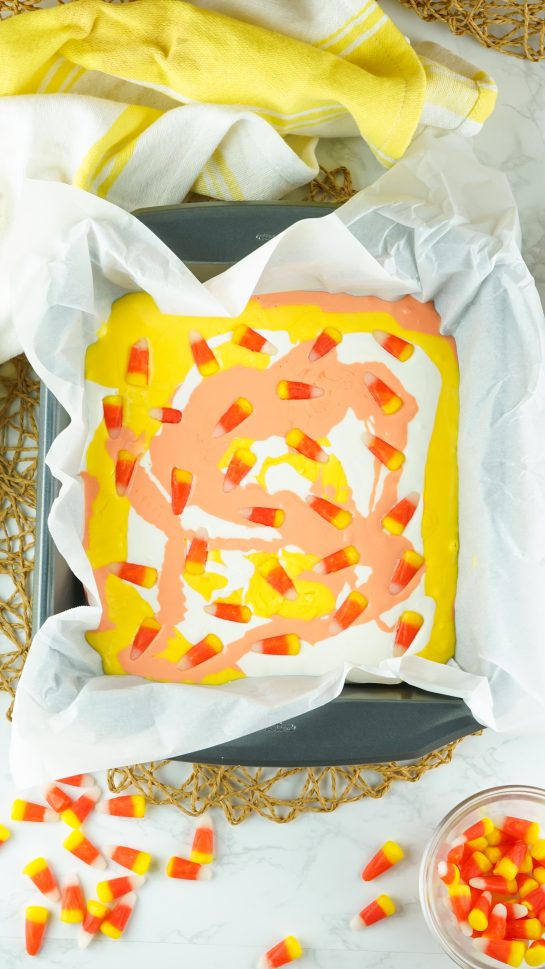 Placing the candy corn on the melted white chocolate needed to make the No-Bake Candy Corn Fudge recipe