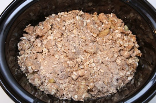 Pouring the streusel topping into the slow cooker to make the Crock Pot Apple Crisp recipe