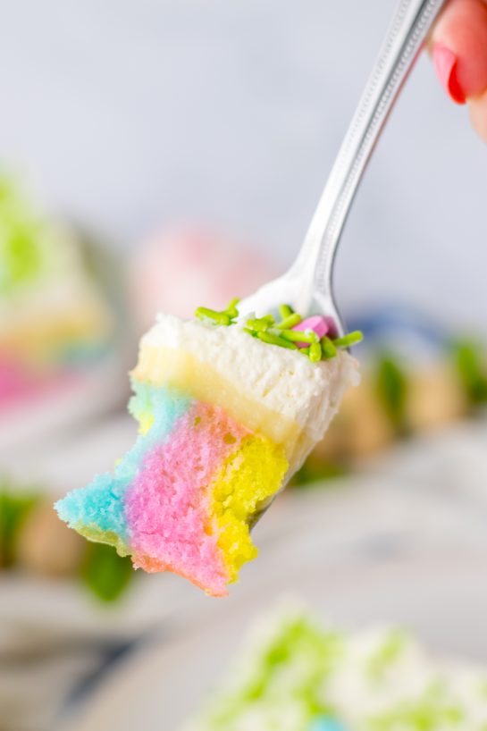 Showing a bite-size piece of the finished Easter Poke Cake on a recipe on a fork, ready to eat.