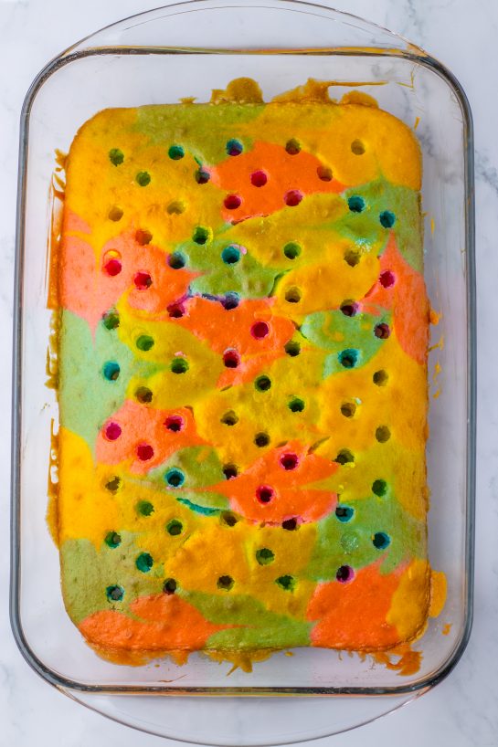 Poking holes in the colored batter for the Easter poke cake recipe after it comes out of the oven.