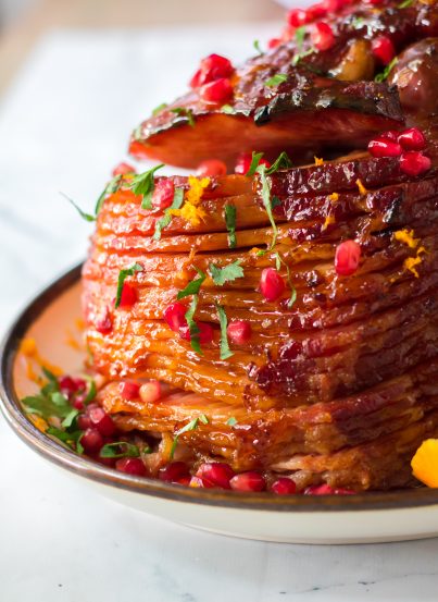 It isn’t Christmas without a gorgeous, glazed Christmas ham recipe and this one is perfect!  Orange juice, brown sugar, honey and cinnamon make up a delicious glaze for this ham.  Orange zest, pomegranate seeds and parsley give this ham it’s festive colors.  This ham smells and tastes like Christmas Day and is sure to become your new holiday ham.