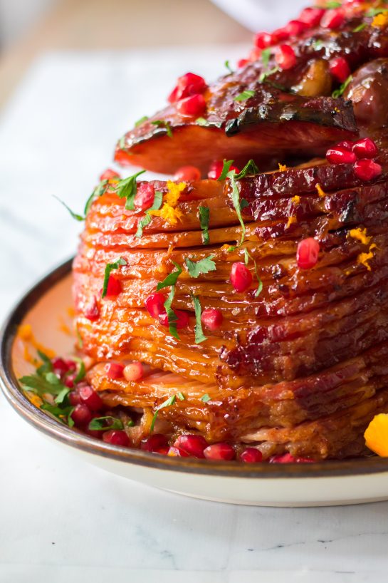 It isn’t Christmas without a gorgeous, glazed Christmas ham recipe and this one is perfect!  Orange juice, brown sugar, honey and cinnamon make up a delicious glaze for this ham.  Orange zest, pomegranate seeds and parsley give this ham it’s festive colors.  This ham smells and tastes like Christmas Day and is sure to become your new holiday ham.