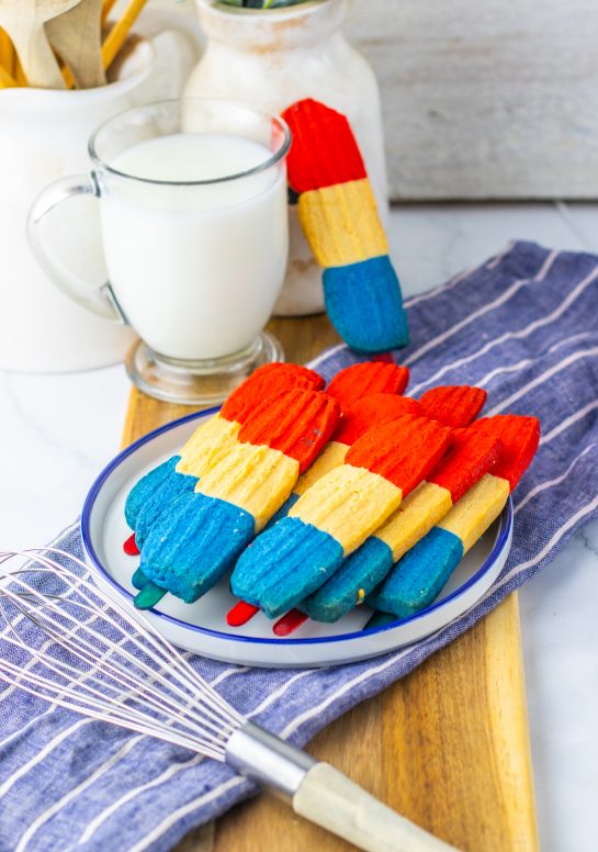 This recipe for Bomb Pop Cookies is not only so tasty but so cute for the 4th of July! These are the perfect dessert to bring for those red, white and blue holidays. Bursting with Sugar cookie flavors with hints of cherry flavoring in the red and blueberry flavoring in the blue, using Jello! These were so fun to make and were a huge hit for your outdoor parties and picnics!
