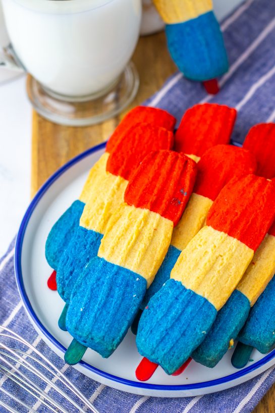 This recipe for Bomb Pop Cookies is not only so tasty but so cute for the 4th of July! These are the perfect dessert to bring for those red, white and blue holidays. Bursting with Sugar cookie flavors with hints of cherry flavoring in the red and blueberry flavoring in the blue, using Jello! These were so fun to make and were a huge hit for your summer picnic!