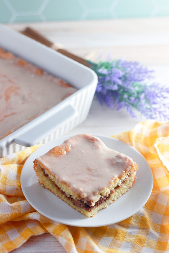 Easy Honey Bun Cake recipe made with yellow cake mix, sour cream, and chopped pecans is a Southern-inspired dessert that tastes just like a warm bakery honey bun! Perfectly moist, swirled with brown sugar and cinnamon, and topped with a sweet glaze, this easy doctored cake mix recipe comes together in minutes — no fancy baking skills required.